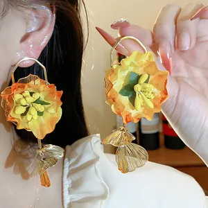 Exaggerated floral dangle earrings with fabric petals and golden metallic charms on model