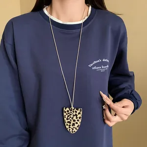 Detailansicht einer Halskette mit Leopardenmuster und Kunstlederanhänger auf blauem Pullover.
