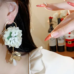 Close-up detail of elegant white fabric flower earrings with gold leaf accents on ear.