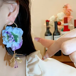 Close-up detail of oversized blue fabric flower earring with gold leaves and purple crystal