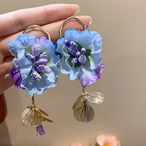 Close-up detail of large blue fabric flower earrings with purple beads and gold dangles