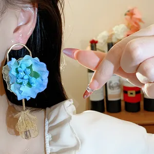 Detail view of oversized blue fabric flower earring with gold petal dangle on ear