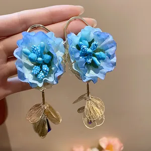 Close-up detail of elegant blue fabric flower earrings featuring hanging golden leaf petals