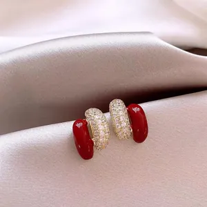 Primo piano di eleganti orecchini a lobo in smalto rosso e pavé di diamanti su raso