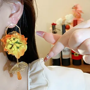 Close-up view of elegant orange fabric flower earrings with glass drop beads on model