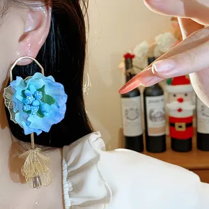 Close-up of an oversized blue fabric flower earring with gold-tone leaf dangles