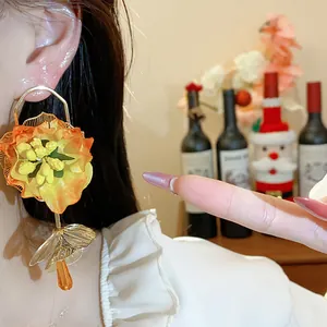 Macro shot of stylish orange fabric flower earring with golden petals and teardrop bead