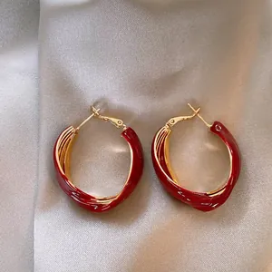 Primo piano dei dettagli degli orecchini a cerchio intrecciati in smalto rosso e oro