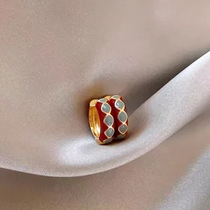 Dettaglio ravvicinato di orecchini a cerchio vintage in smalto rosso con motivi grigi.