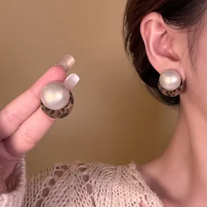 Close-up of a pearl stud earring with a stylish leopard print accent on a model's ear.