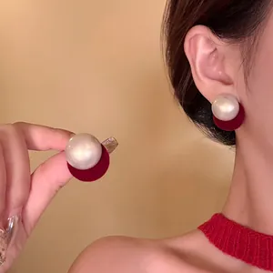 Detail view of elegant pearl stud earrings with red velvet backing on a female model