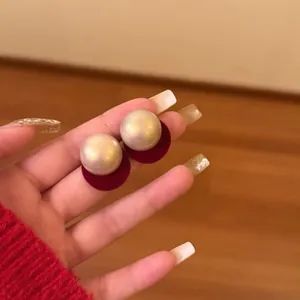 Close-up detail of elegant round pearl stud earrings featuring red velvet base on hand
