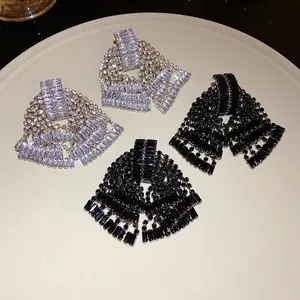 Detailed view of silver and black rhinestone bow tassel earrings on white plate.