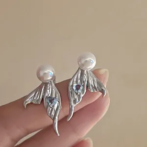 Close-up detail of silver mermaid tail stud earrings with heart blue zircon and white pearl