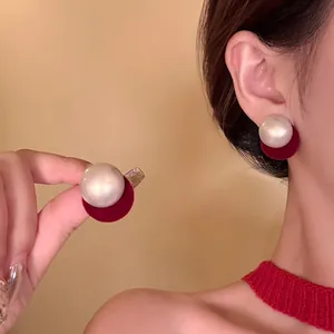 Close-up of minimalist round pearl earrings with red velvet backing on model's ear
