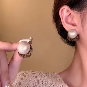 Detail of leopard print pearl earrings worn on ear and held by hand