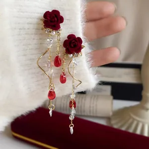 Dettaglio di orecchini a rosa in velluto rosso con perle e cristalli su maglione bianco.