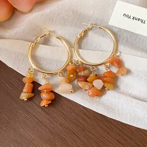 Close-up of gold hoop earrings featuring irregular orange natural stone tassels.