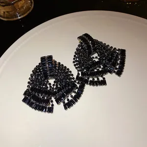 Detailed close-up of elegant black crystal bow earrings with tassel drops on a white plate