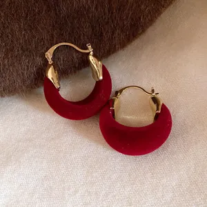 Dettaglio ravvicinato di eleganti orecchini a cerchio in velluto rosso e finiture in oro