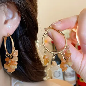 Detailed view of golden hoop earrings featuring irregular orange stone tassels