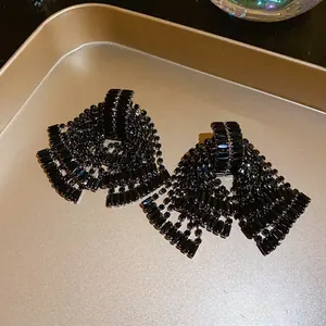 Close-up detail of elegant black rhinestone bow tassel earrings on a metallic tray