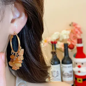 Close-up of gold hoop earrings with irregular orange stone tassels on model ear.