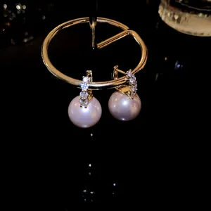 Elegant pink pearl drop earrings with sparkling stone inlay on gold-tone hoops. Macro view.