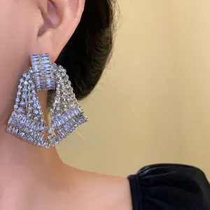 Detailed view of oversized sparkly silver-tone rhinestone statement earrings on ear.