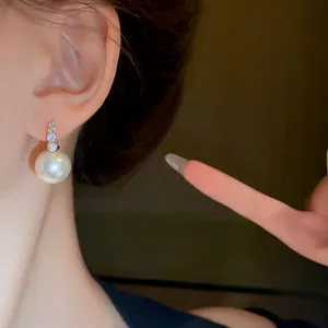 Close-up of elegant white pearl earring with sparkling rhinestones worn on ear lobe