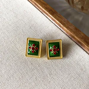 Detailansicht von quadratischen Vintage-Ohrsteckern mit grüner Emaille und roten Kristallen.