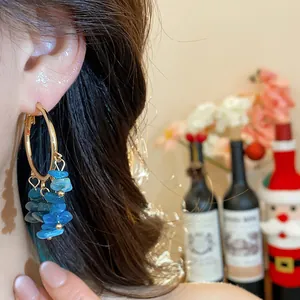 Detailed view of golden hoop earrings featuring vibrant irregular blue stone tassels