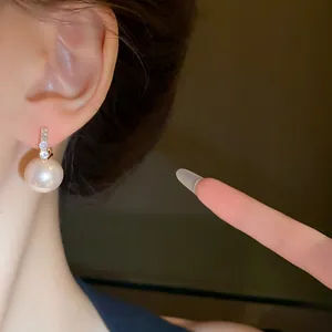 Close-up of elegant pink pearl earrings with shimmering diamond details worn on ear.