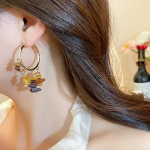 Close-up of gold hoop earrings with irregular colorful stone tassels on model's ear.