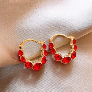 Macro detail of luxury gold hoop earrings with sparkling red crystals on satin background