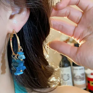 Close-up detail of gold hoop earrings featuring irregular blue stone tassels worn by a model