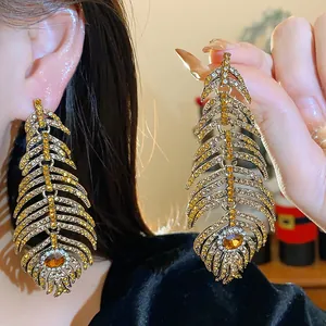 Detail of gold feather earrings with sparkling rhinestones held for close-up view