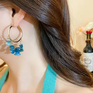 Macro view of a gold hoop earring featuring irregular blue stone tassels worn by a model