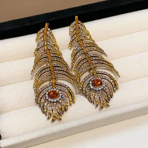 Detailed view of ornate gold-tone feather earrings encrusted with yellow rhinestones