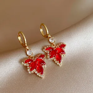 Detailed view of elegant gold-toned earrings featuring vibrant red crystal maple leaf charms