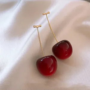 Close-up of elegant red cherry-shaped earrings on soft white fabric background