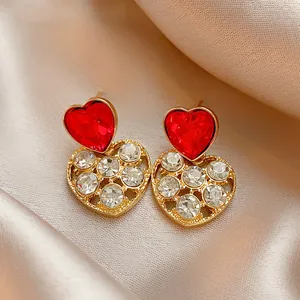 Detailed macro close-up of red heart-shaped earrings with white rhinestone accents on satin.
