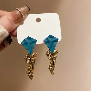 Close-up of geometric earrings with matte teal rhombus and crumpled gold foil texture