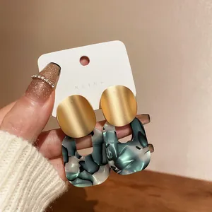 Close-up detail of vintage geometric earrings with gold studs and green marbled resin drops