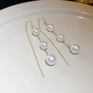 Close-up of elegant gold threader earrings featuring three lustrous white pearls
