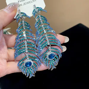 Macro detail of luxurious peacock feather earrings encrusted with blue and green rhinestones