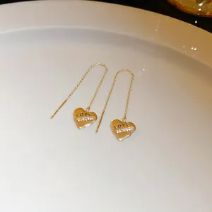 Detailed close-up of gold heart threader earrings with LOVE engraving and tiny rhinestones