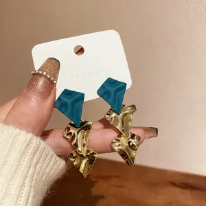 Close-up detail of vintage geometric earrings with teal matte and hammered gold finish