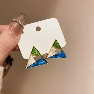 Close-up of geometric triangle earrings with vibrant green, blue, and white resin panels