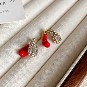Detailed close-up of red enamel and sparkling rhinestone teardrop earrings in display tray